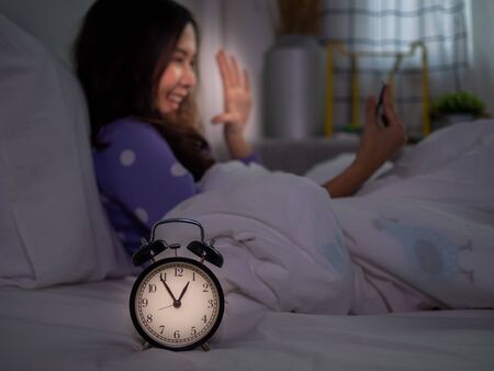 An Asian woman is using a smartphone to make video calls with her boyfriend in bed before going to bed at night. Smartphone addictionの写真素材