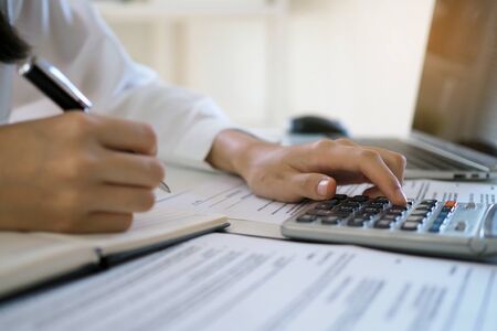 Asian businessmen work with calculators to calculate account information. In the office, work desks with documents and computersの写真素材