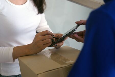 Good tempered woman signed on the smartphone to receive parcels from the sender. Fastest online deliveryの写真素材