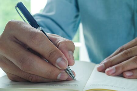 Image of male hand focusing holding a pen to write.  Businessman writing on paper report in office.の写真素材