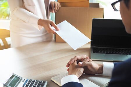The business woman has a brown cardboard box next to her body and sends a letter of resignation to the executive. Include about resignation, job placement and vacancies.の写真素材