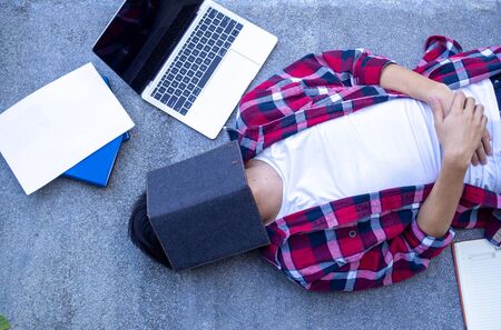 Stressed student with book cover his face. Relaxing, lazy, tired from reading exam preparation books.の写真素材