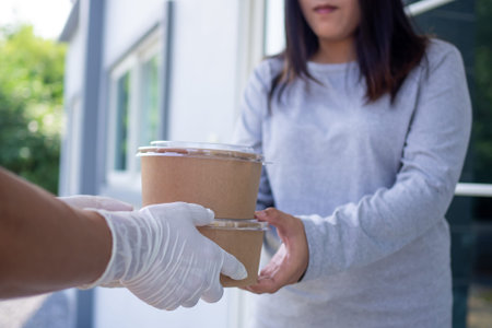 Deliveryman wearing gloves delivers food boxes to customers.  Woman hand accepting delivery of boxes...