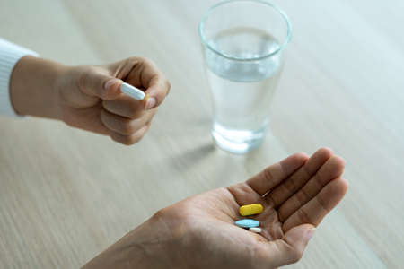 a woman holding a food supplement or medication with a glass of water on the table. Medical concepts and health care, illnessの写真素材