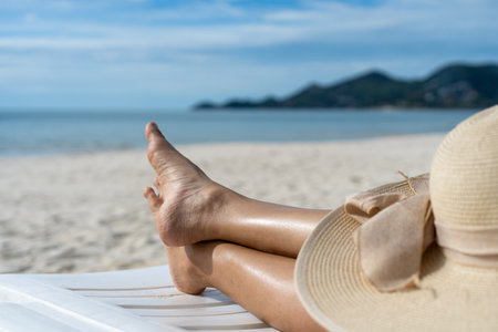 woman's feet is sitting on a beachside chair with a hat. good location at the sea with beach chairs. Summer holiday conceptの写真素材