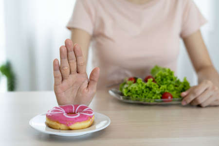 Good health food and diet. Women reject junk food or unhealthy foods such as doughnuts and choose healthy foods such as salads.の写真素材