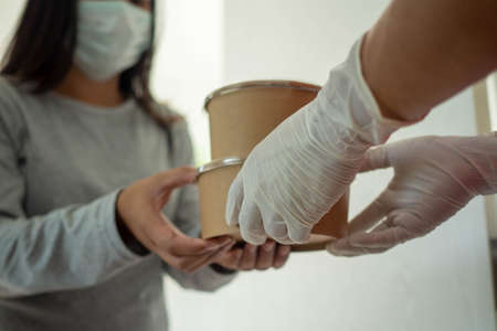 The food deliveryman wearing gloves carries a food box send to customers at  home During the outbreak of COVID 19.の写真素材