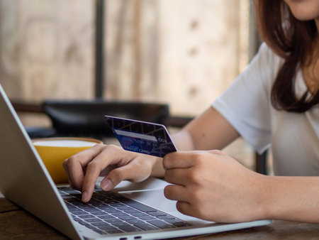 Young woman is using a smartphone to pay for goods by credit card while shopping online on a laptop. Online shopping conceptの写真素材