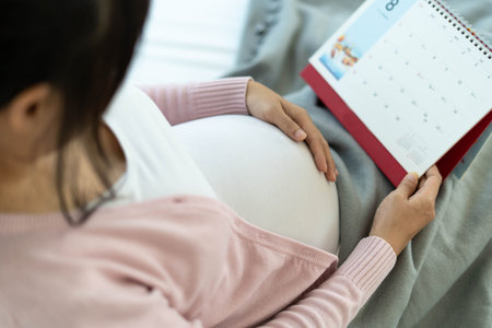 A pregnant woman touches her belly with her hand and looks at the date of birth on the calendar.