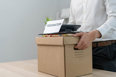 A businessman holds a box for personal items after sending a resignation letter to an executive or manager. Include information about resignation and vacancies and job changes.の写真素材