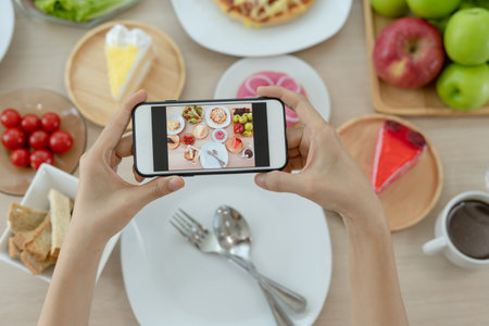 A man uses a mobile phone to open an app to take pictures of food at a table in a restaurant.の写真素材