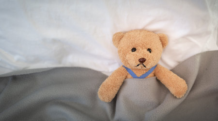 A sad teddy bear lies sick in bed with disappointment and discouragementの写真素材
