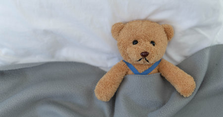 A sad teddy bear lies sick in bed with disappointment and discouragement