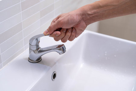 The faucet in the bathroom with running water. Man keeps turning off the water to save water energy...