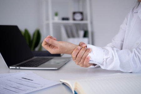 Businesswoman hurts wrist while working. A woman uses a computer for a long time causing Trigger Finger. Office Syndrome Concept.の写真素材