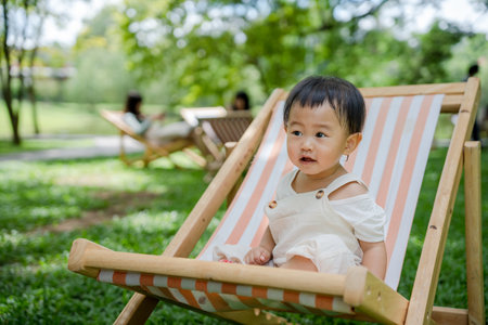 children asian girl is sitting on chair on the lawn. Brightly smiling daughter relax or recreation with her family on vacation. tourism trip with summer cafes. happiness, laughter, childhood learningの写真素材