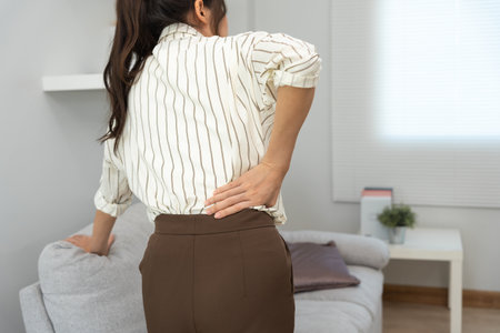 Asia beautiful woman holding her lower back while and suffer from unbearable pain health and problems, chronic back pain, backache in office syndrome, scoliosis, herniated disc, muscle inflammationの写真素材