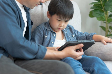 Happy single father playing teach using tablet with the little boy. family is happy and excited in the house. Father and son having spending time together, Good daddy , addiction fix, handle, controlの写真素材
