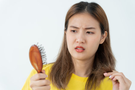 Asian woman very sad and upset looking at damaged hair, hair loss, hair thinning problem, vitamin deficiency, baldness, postpartum, biotin, zinc, menstrual or endocrine disorders, hormonal imbalanceの写真素材