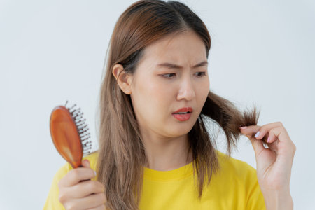 Asian woman very sad and upset looking at damaged hair, hair loss, hair thinning problem, vitamin deficiency, baldness, postpartum, biotin, zinc, menstrual or endocrine disorders, hormonal imbalanceの写真素材