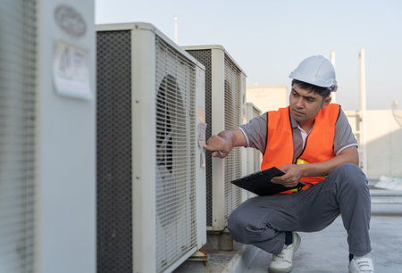 Asian maintenance engineer works on the roof of factory. contractor inspect compressor system and plans installation of air condition systems in construction. Checklist, inspector, controlの写真素材