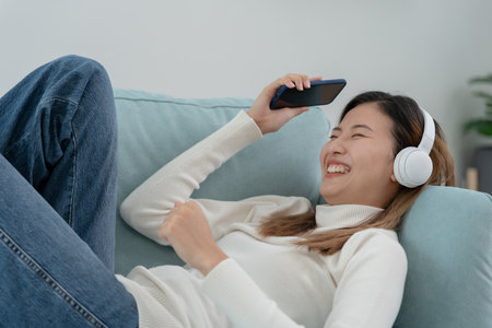 Joyful young Asian women in wireless headphones sitting and enjoy music, having fun, listening to music, raising his arm, dancing to favorite song, enjoying cool soundtrack, happy life, recreationの写真素材