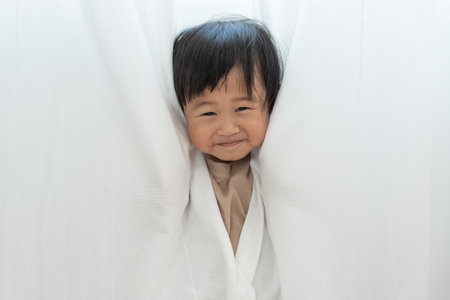 little asian children kid girl covering his eyes with hands, playing hide and seek standing next a wall house, Adorable child having fun in the home. happy family have fun with kids, activity, learningの写真素材