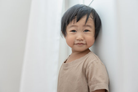 little asian children kid girl covering his eyes with hands, playing hide and seek standing next a wall house, Adorable child having fun in the home. happy family have fun with kids, activity, learningの写真素材