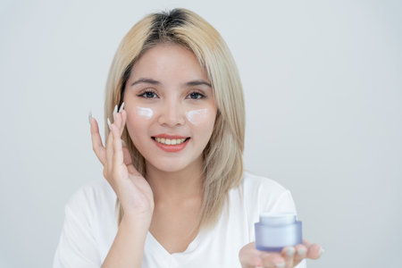 Beautiful Asian woman sit in front of a mirror. face of a healthy woman applying cream and makeup. Advertisement for skin cream, anti-wrinkle, baby face, whitening, moisturizer, tighten pores serumの写真素材