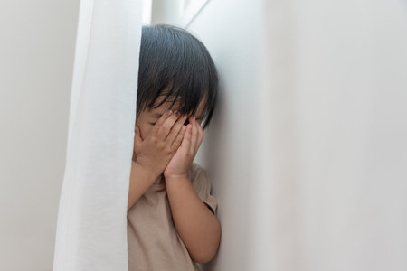 little asian children kid girl covering his eyes with hands, playing hide and seek standing next a wall house, Adorable child having fun in the home. happy family have fun with kids, activityの写真素材