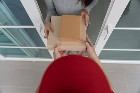 woman receives boxes parcel from courier in front house. Delivery man send deliver express. online shopping, paper containers, takeaway, postman, delivery service, packagesの写真素材