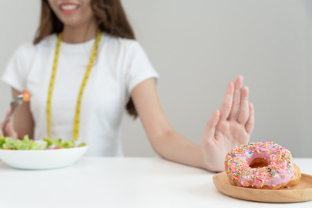 Diet and dieting. Beauty slim female body confuse donut. Woman in exercise clothes achieves weight loss goal for healthy life, crazy about thinness, thin waist, nutritionist.の写真素材