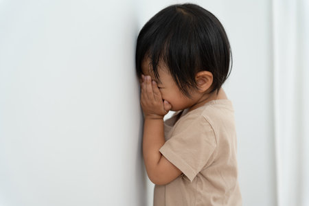 little asian children kid girl covering his eyes with hands, playing hide and seek standing next a wall house, Adorable child having fun in the home. happy family have fun with kids, activity, learningの写真素材