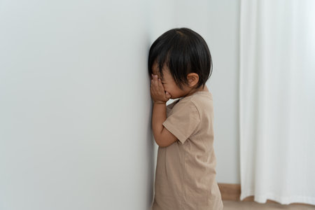 little asian children kid girl covering his eyes with hands, playing hide and seek standing next a wall house, Adorable child having fun in the home. happy family have fun with kids, activityの写真素材