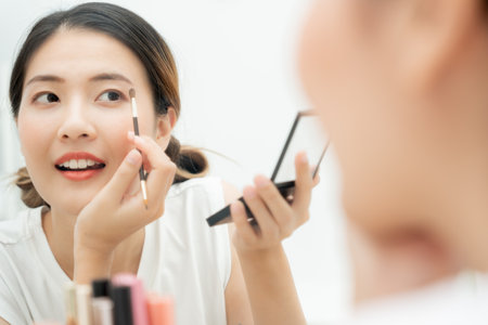 Beautiful Asian woman sit in front of a mirror and smile on makeup. face of a healthy woman applying makeup. Advertisement, lifestyle , cosmetics, makeup accessories, beauty activity, beauticianの写真素材