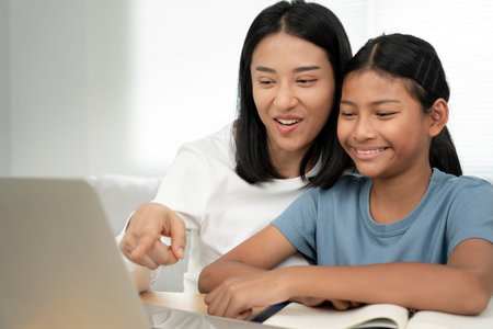 Mother teaching lesson for daughter by laptop. Mother and child laughing happily. Do homework with...