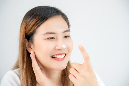 Beautiful Asian woman smile use cream touch on nose skin. face of a healthy woman apply cream and makeup. Advertisement for skin cream, anti-wrinkle, baby face, whitening, moisturizer, tighten poresの写真素材