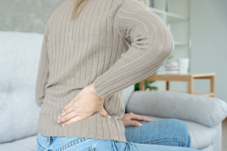 Asia beautiful woman holding her lower back while and suffer from unbearable pain health and problems, chronic back pain, backache in office syndrome, scoliosis, herniated disc, muscle inflammationの写真素材