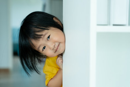 little asian children kid playing hide and seek standing next wall house, Adorable child having fun in the home. happy family have fun with kids, activity, learning, activity, game, meditationの写真素材