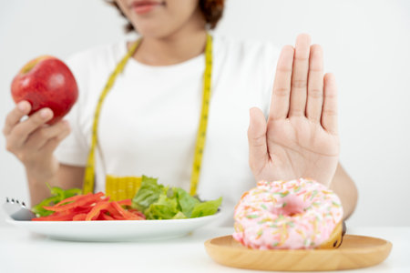 Diet and dieting. Beauty slim female body confuse donut. Woman in exercise clothes achieves weight loss goal for healthy life, crazy about thinness, thin waist, nutritionist.の写真素材
