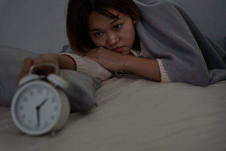 asian woman in bed late trying to sleep suffering insomnia, sleepless or scared in a nightmare, looking sad worried and stressed. Tired and headache or migraine waking up in the middle of the night.の写真素材
