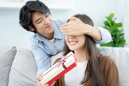 Asian couples are about to do a surprise with their wives on their wedding anniversary. Teenage husband and wife after marriage. Happiness and smiles and laughter in warm family. cuddling, warm hugsの写真素材