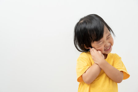 little asian girl presses hand to cheek, suffers from pain in tooth. Teeth decay, dental problems, child emotions and facial expression, oral health care, reducing sweets, fluorine coatingの写真素材