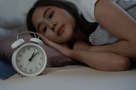 asian woman in bed late trying to sleep suffering insomnia, sleepless or scared in a nightmare, looking sad worried and stressed. Tired and headache or migraine waking up in the middle of the night.の写真素材
