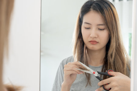 Asian woman very sad and upset looking at damaged hair, hair loss, hair thinning problem, vitamin deficiency, baldness, postpartum, biotin, zinc, menstrual or endocrine disorders, hormonal imbalanceの写真素材
