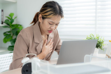 hand hold chest with heart attack symptoms, asian woman working hard have chest pain caused by heart disease, leak, dilatation, enlarged coronary heart, press on the chest with painful expressionの写真素材
