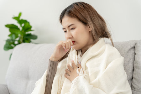 sick woman with a headache sitting under blanket, female sneezing and runny nose with seasonal influenza, allergic, high fever and influenza, resting, virus, coronavirus, feel illness, respiratoryの写真素材