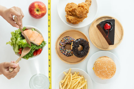 Woman choose healthy food for diet. Healthy food and fatty food separated on table with measuring tape. Lose weight, balance, control, reduce fat, low calorie, routine, exercise, body shape.の写真素材
