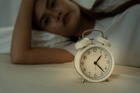 asian woman in bed late trying to sleep suffering insomnia, sleepless or scared in a nightmare, looking sad worried and stressed. Tired and headache or migraine waking up in the middle of the night.の写真素材