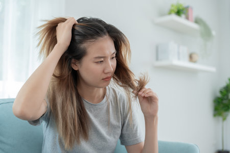 Asian woman very sad and upset looking at damaged hair, hair loss, hair thinning problem, vitamin deficiency, baldness, postpartum, biotin, zinc, menstrual or endocrine disordersの写真素材